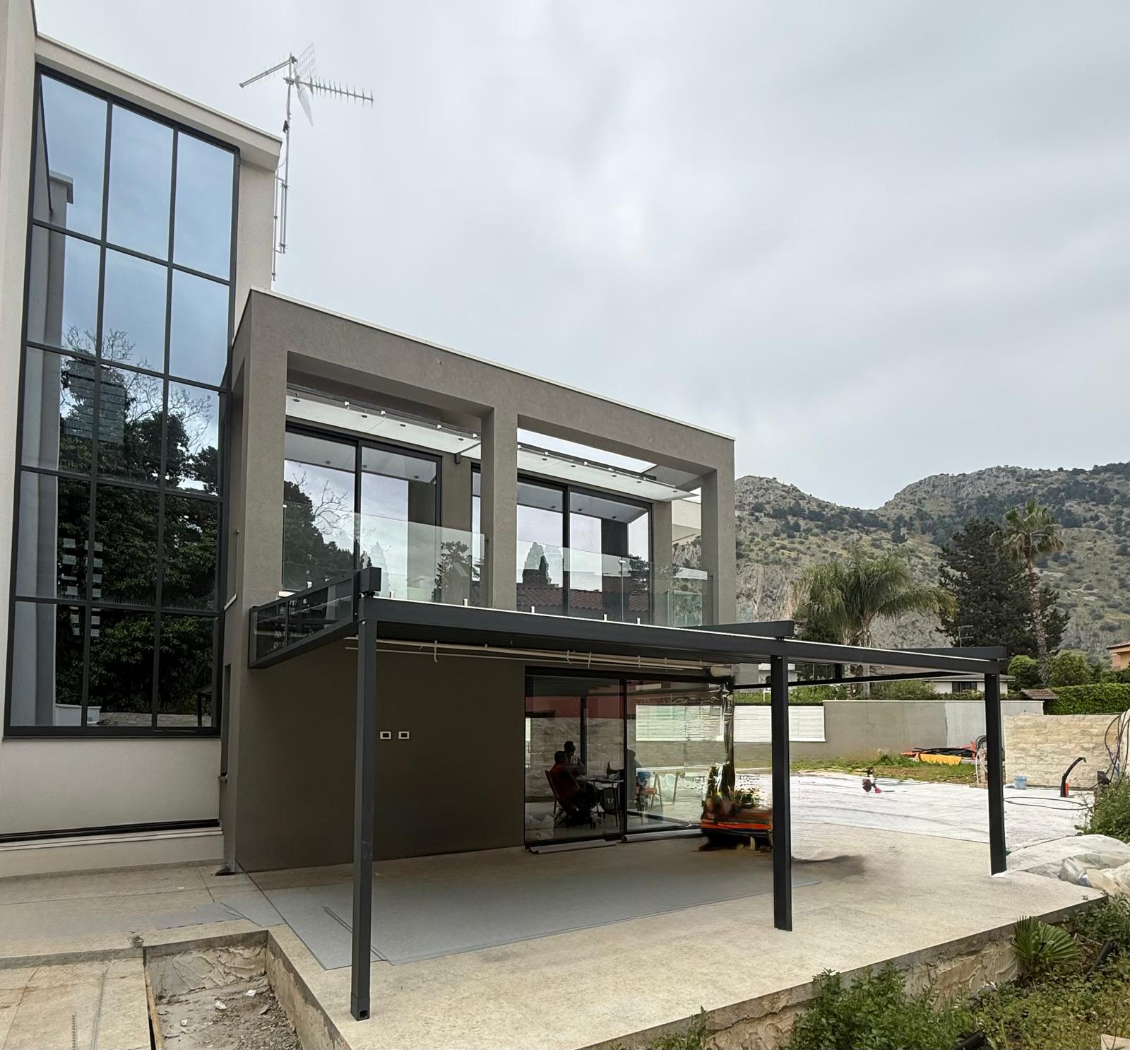 Pergola bioclimatica antracite vista laterale su villa con parapetto in vetro